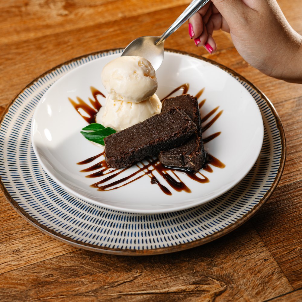 Sobremesa do Ponto do Peixe: brownie com sorvete e calda, servido em prato de porcelana.