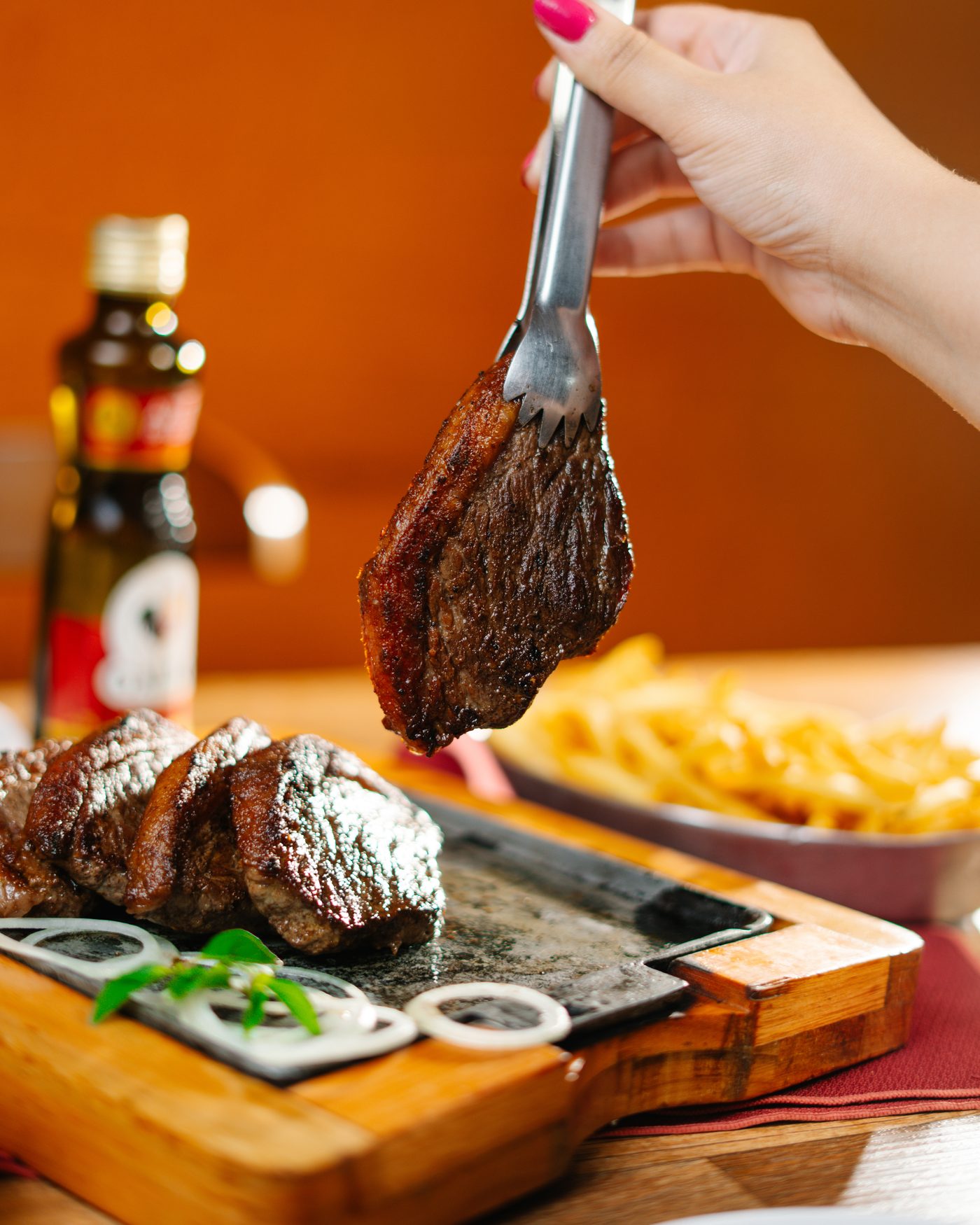 Picanha fatiada na chapa de pedra com batatas fritas ao fundo
